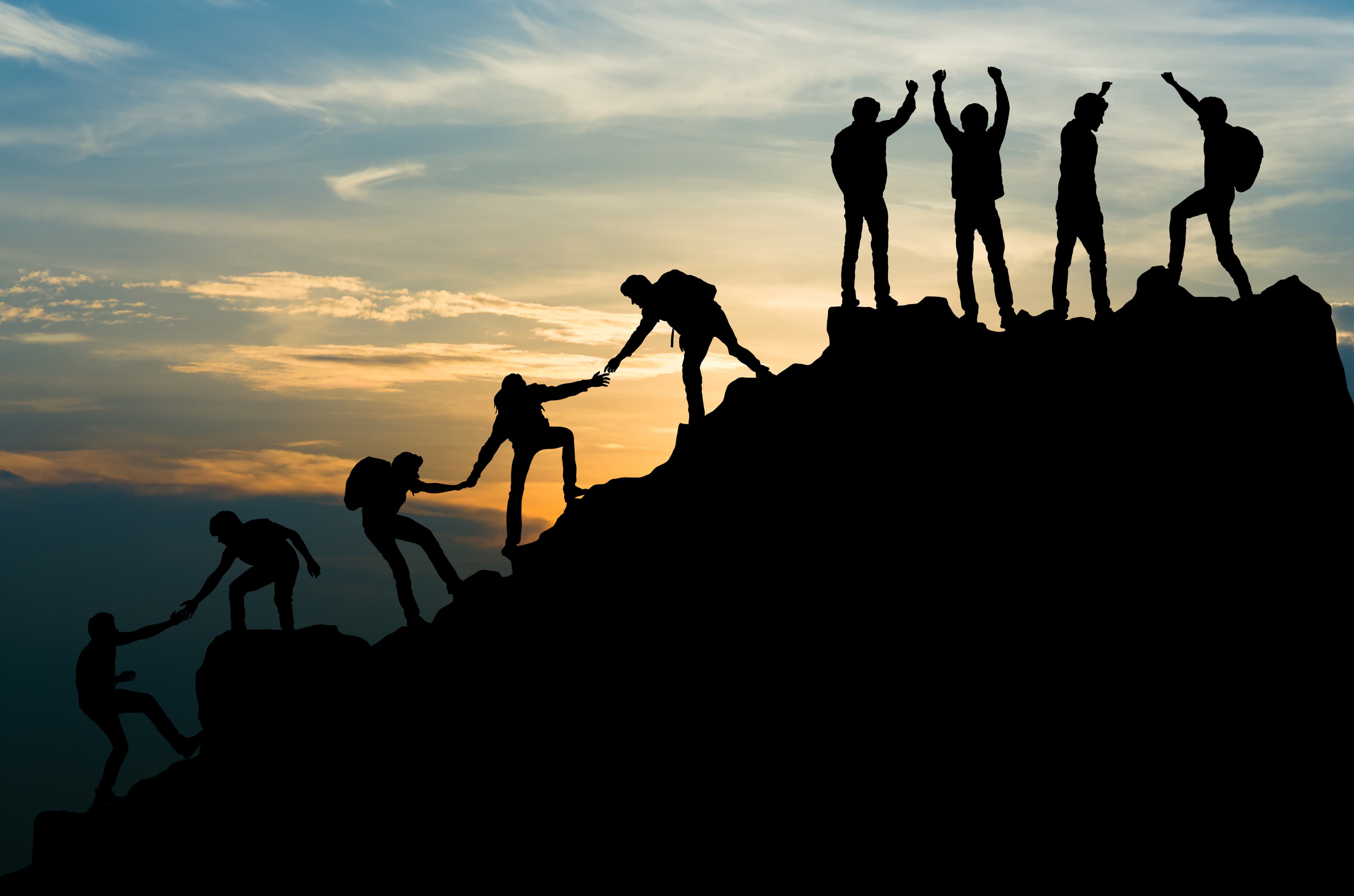 Group of people on peak mountain climbing helping team reach the top