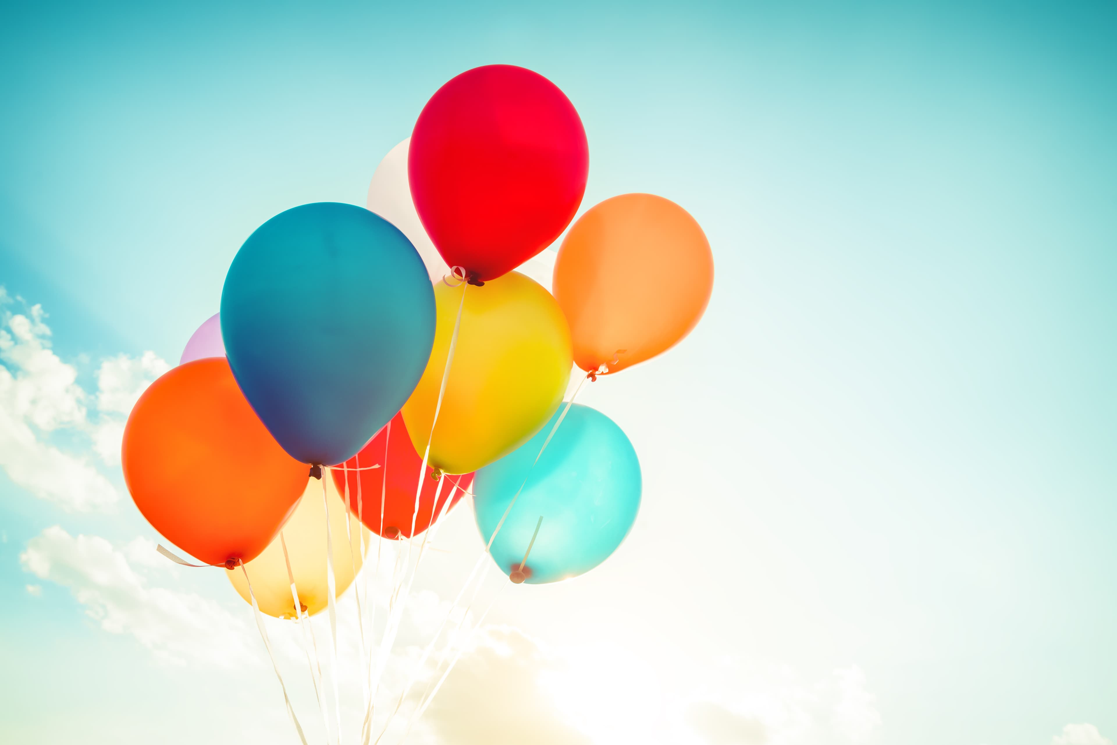 Balloons floating up into a blue sky with white clouds