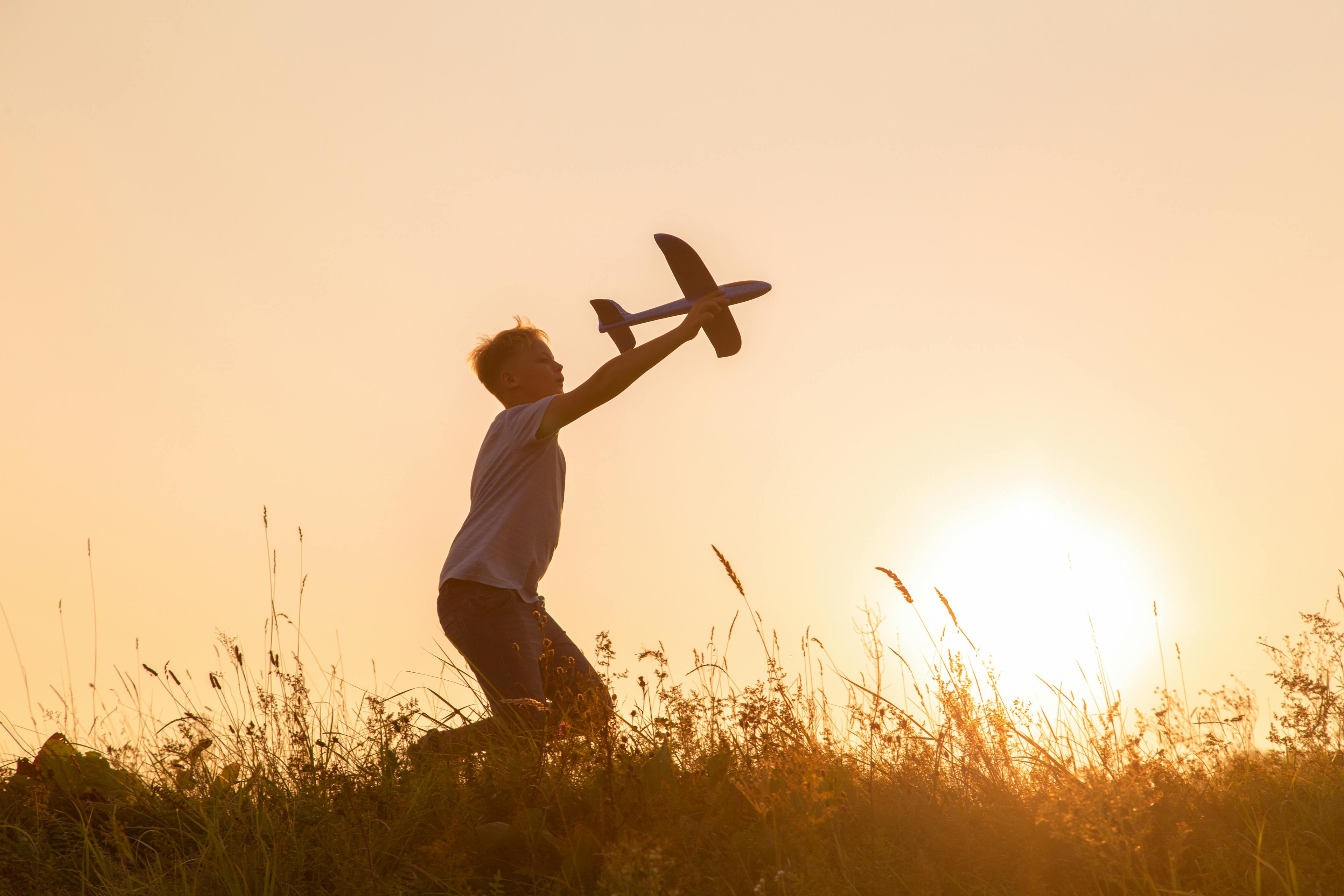 Boy playing with model plane at sunset