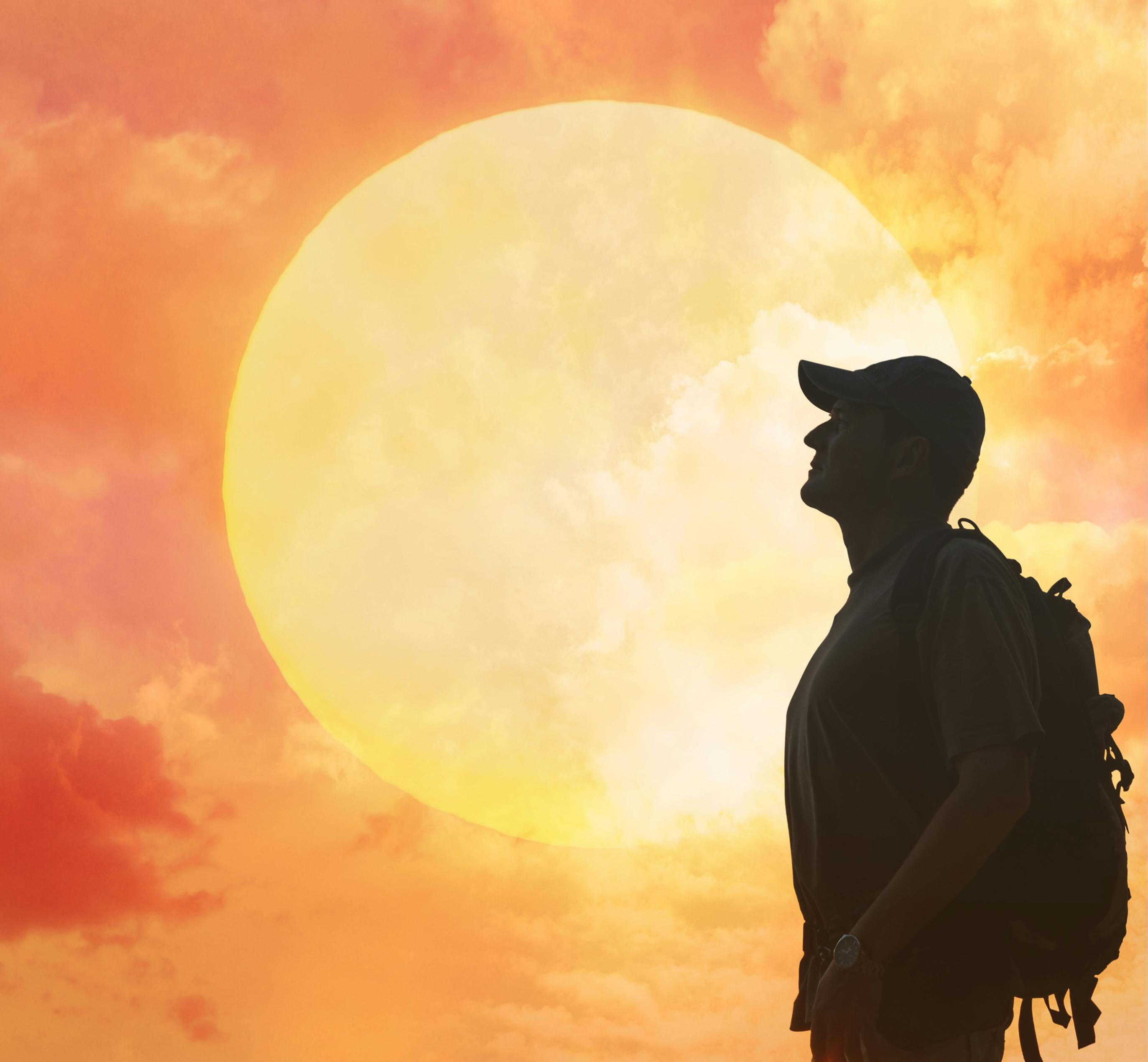 Silhouette of man with backpage in front of orange sun